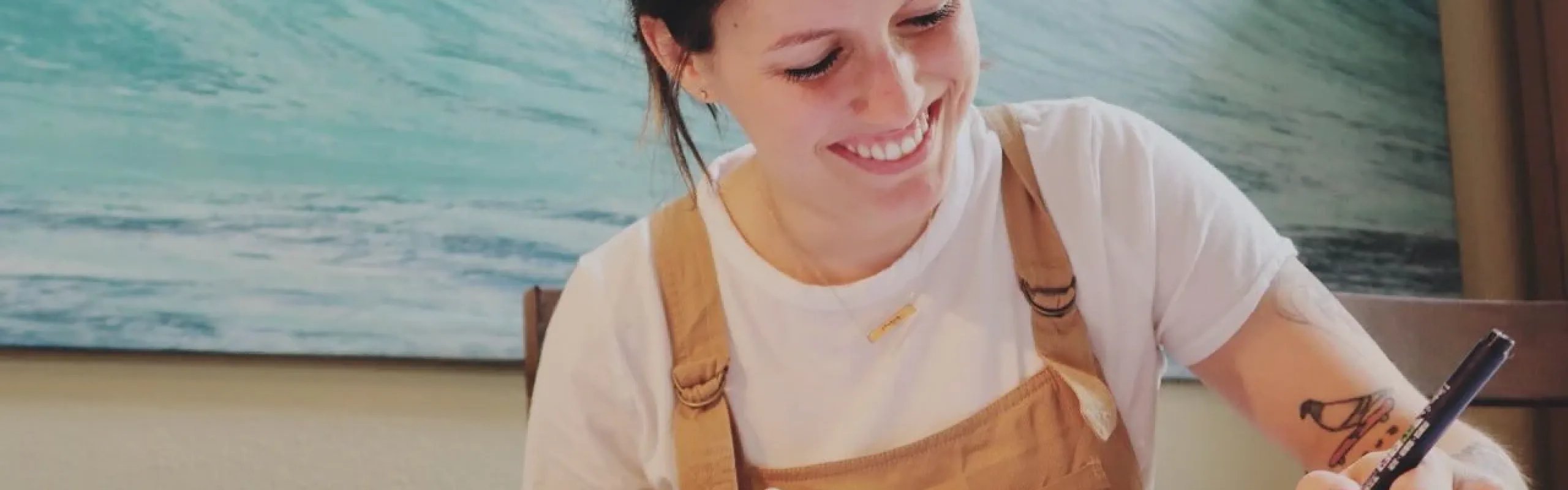 Peggy Dean smiling as she letters at a table.